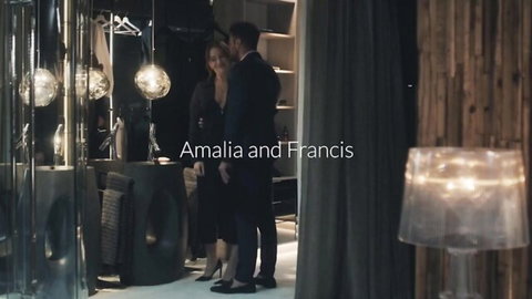 Sexy brunette in low-cut dress stands intimately with suited man in luxurious bedroom