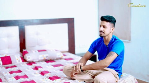 Indian man in blue shirt sits calmly on bed in cougar affair video