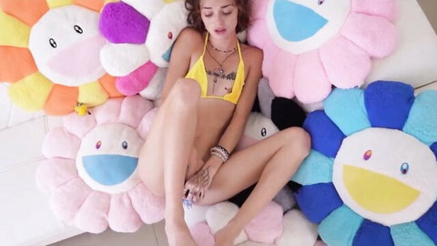 Petite babe in yellow bikini spreads legs wide and fingers exposed shaved pussy amid giant colorful flower pillows