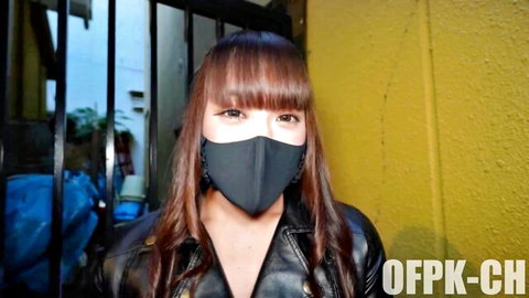 Sexy Asian woman in black leather jacket and mask teasing with cleavage outdoors