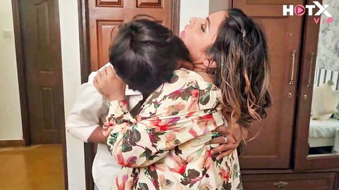 Sexy South Asian MILF in open floral robe passionately hugs and neck-kisses young man showing deep cleavage