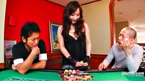 Sexy Asian woman in black corset and gloves deals poker chips to two clothed men at table