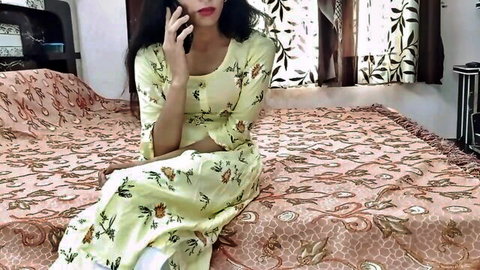 Indian Desi Hancock in yellow floral dress, sitting on bed seductively