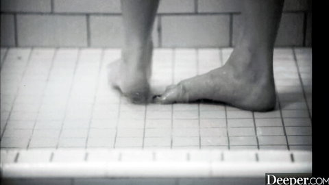 Closeup of bare feet standing on wet shower tiles in steamy black and white scene