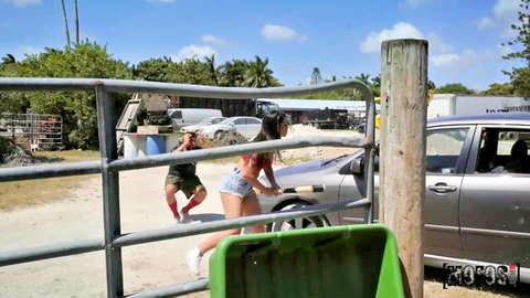Katana Kombat in red bikini bending over car during outdoor wash with Oliver Flynn