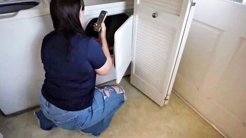 Curvy brunette in ripped jeans kneels at washer, teasing big ass view