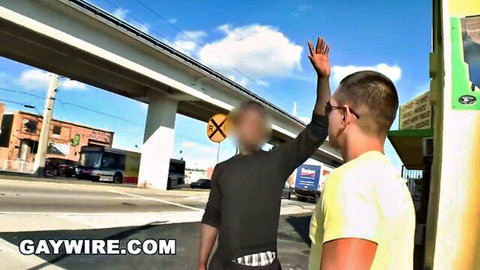 Two blurred gay guys in tight clothes walking and waving on sunny urban street under bridge