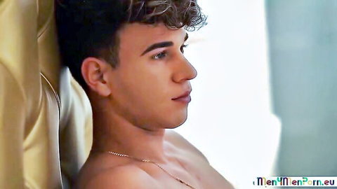 Handsome shirtless curly-haired gay twink in seductive side profile on golden couch