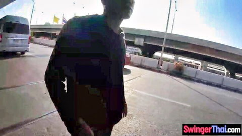 Amateur Thai man walking on busy street near buses under bridge towards camera