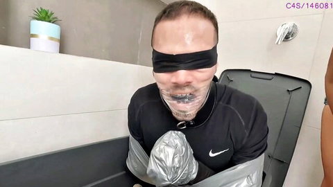 Blindfolded gagged man bound with duct tape in bathtub BDSM slave scenario