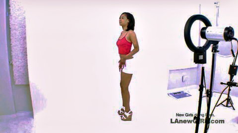 Nina Elle in red tank top and white shorts posing sideways for audition, curvy black model