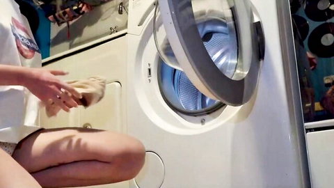 Stepsis in pink panties squatting by open washer, holding cloth