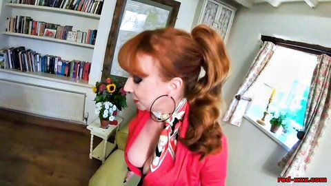 Busty redhead in low-cut red dress teasing massive cleavage in cozy living room