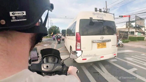 Motorcyclist in helmet follows white Toyota van in busy Thai street traffic