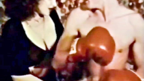 Busty retro babe in low-cut top showing cleavage next to muscular shirtless boxer with red gloves