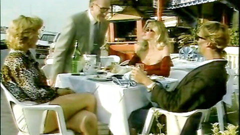 Busty blonde MILF in red dress teasing at outdoor table with men
