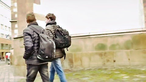 Two young men walking down urban street wearing jackets backpacks and jeans