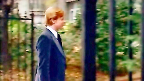 Red-haired young man in navy suit walking near fence, perverted guy in kinky maid scene