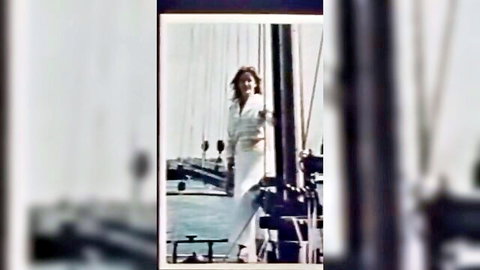 Vintage blonde woman in white dress posing seductively against yacht mast