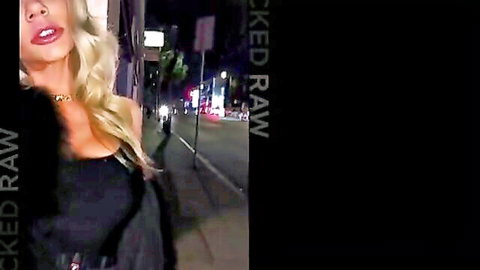 Seductive blonde babe with big tits in tight black dress on neon-lit night street