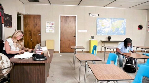 Blonde MILF teacher grading papers at desk in classroom with black students sitting attentively