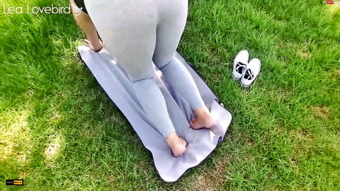 Lea Lovebird in tight gray leggings, bending over in yoga pose outdoors
