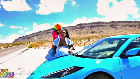 Ebony clown model in rainbow wig poses provocatively on blue sports car hood in desert