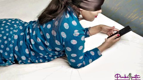 Blindfolded Desi bhabhi in blue dotted kurta lying on bed with phone