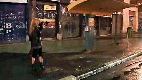 Blonde Brazilian woman in skirt and boots at rainy night bus stop, threesome teaser