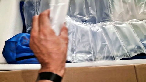Blurry hand gripping translucent bubble wrap packaging over blue bag and cardboard box