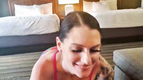 Tattooed brunette MILF smiles seductively with deep cleavage in pink top on hotel room floor