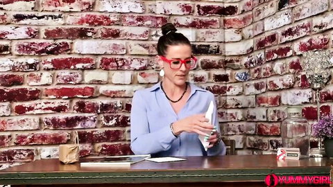 Sexy brunette MILF in glasses and ponytail holds tissue at desk with brick wall background