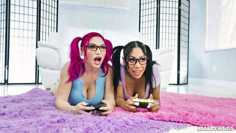 Two busty gamer girls with pigtails and glasses tease big tits in tight tops while playing controllers on rug