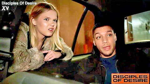 Blonde woman in fur jacket leans intensely toward black man in dark car interior