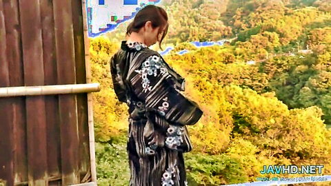 Asian woman in black floral kimono stands sideways in outdoor JAV scene
