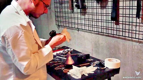 Scientist in lab coat preps BDSM tools for bound humiliation kink
