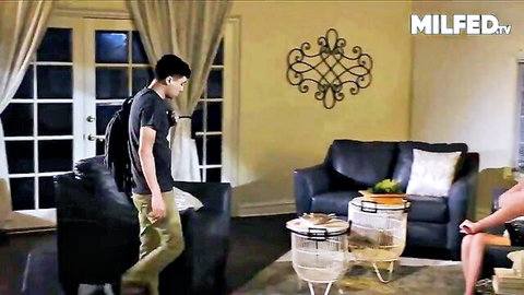 Blonde MILF with huge tits in black dress seduces young guy entering living room