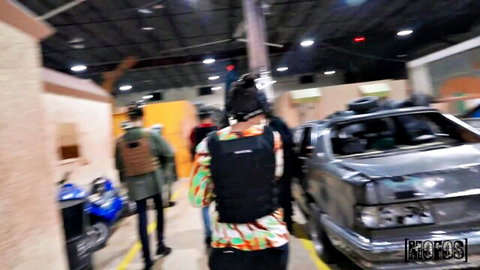 Tactical team in vests and backpacks walking past wrecked cars in warehouse garage
