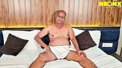 Bald Indian mature man shirtless in towel on bed, teasing daddy vibe