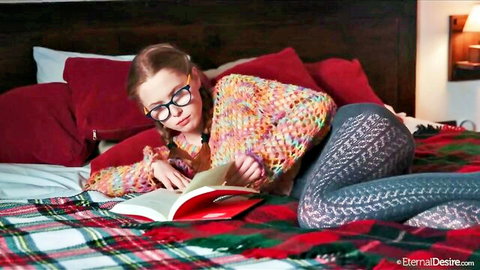 Laura Lit in glasses reading erotically on bed, colorful sweater and tights