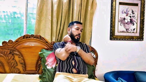 Bearded Indian man in striped shirt lounging on bed, adult thumbnail