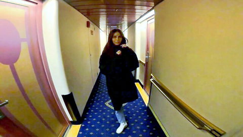 Brunette woman in black coat walks cruise ship hallway, steamy college buddies adventure