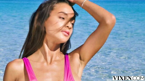 Skinny brunette with small natural tits in tight pink sling bikini poses windblown on beach