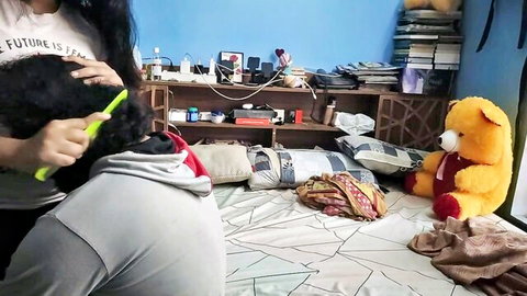 Asian woman in tight leggings brushing small black shih tzu dog on bed in messy bedroom