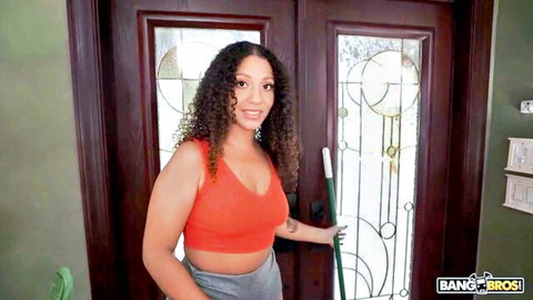 Curly-haired MILF maid in orange tank top and shorts holding broom