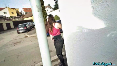 Brunette babe in tight pink tank top and black pants teasing by public pole outdoors