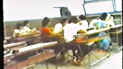 Blurry vintage classroom scene with uniformed students at desks listening to teacher