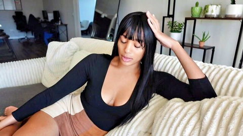 Seductive ebony woman with bangs lounging in low-cut black top and shorts