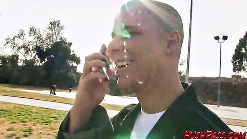 Shaved-head man smiling on phone in sunny outdoor park with lens flare
