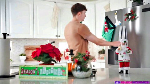 Naked muscular young guy with dangling cock stands in Christmas kitchen holding Santa doll